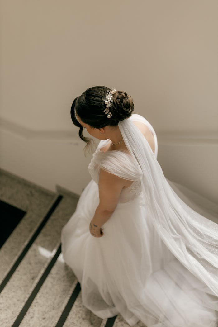 Bride in elegant white gown descending a staircase with a soft, flowing veil.